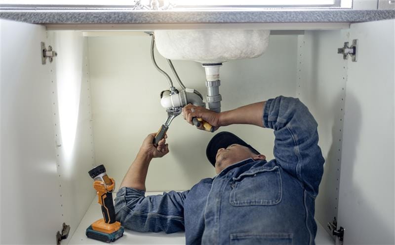 Plumber repairing pipes beneath a bathroom sink in Chula Vista