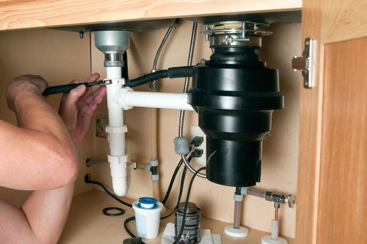 Plumber installing a garbage disposal beneath a kitchen sink in Chula Vista