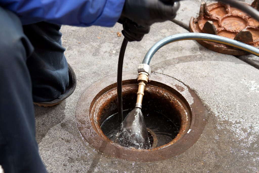 Plumber hydro jetting a sewer line through a manhole in Chula Vista