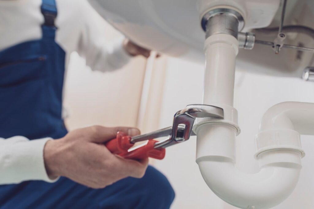 Plumber repairing a white drain pipe beneath a sink in Chula Vista